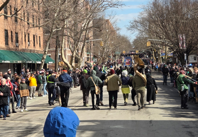 a street-level view from behind a group of musicians marching down a city street lined with spectators during the St. Pats for All parade in Queens
